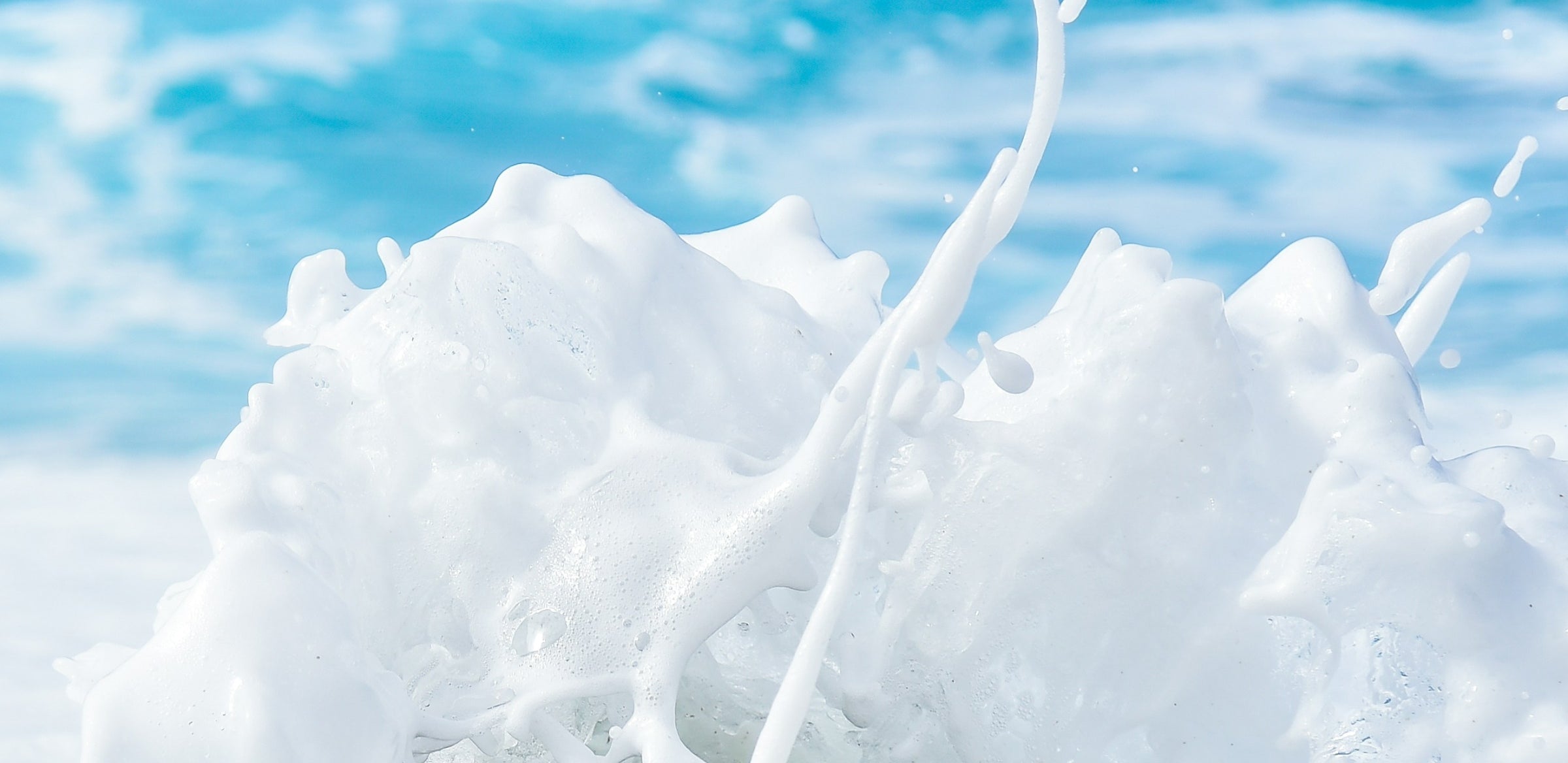 A close-up of white ocean waves splashing, with foamy water droplets spraying upward against a blurred blue sea background—fresh takes on water breaks.