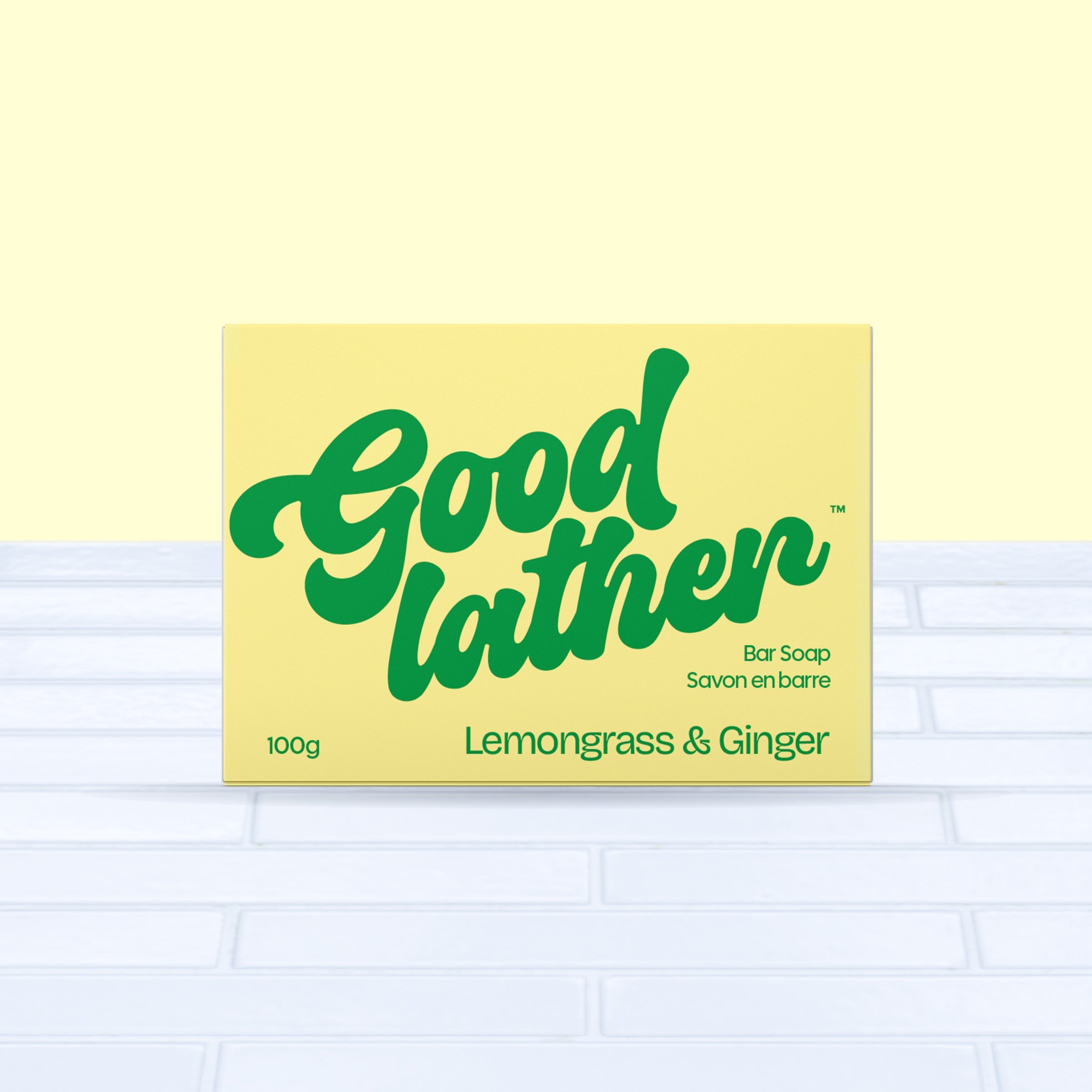 A bright yellow and green box of Goodlather Lemongrass and Ginger Bar Soap, 100g, sits on light blue tiles with a pale yellow backdrop—a sustainable Canadian soap.