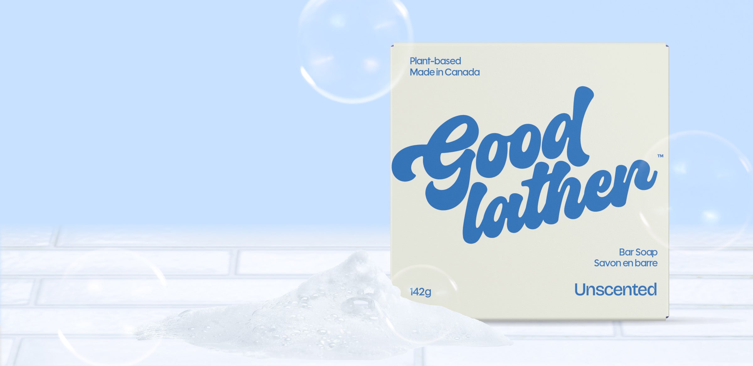 A bar soap package labeled Goodlather bars sits on a light surface with bubbles, against a soft blue background. The box highlights natural ingredients, plant-based, made in Canada, and unscented features.