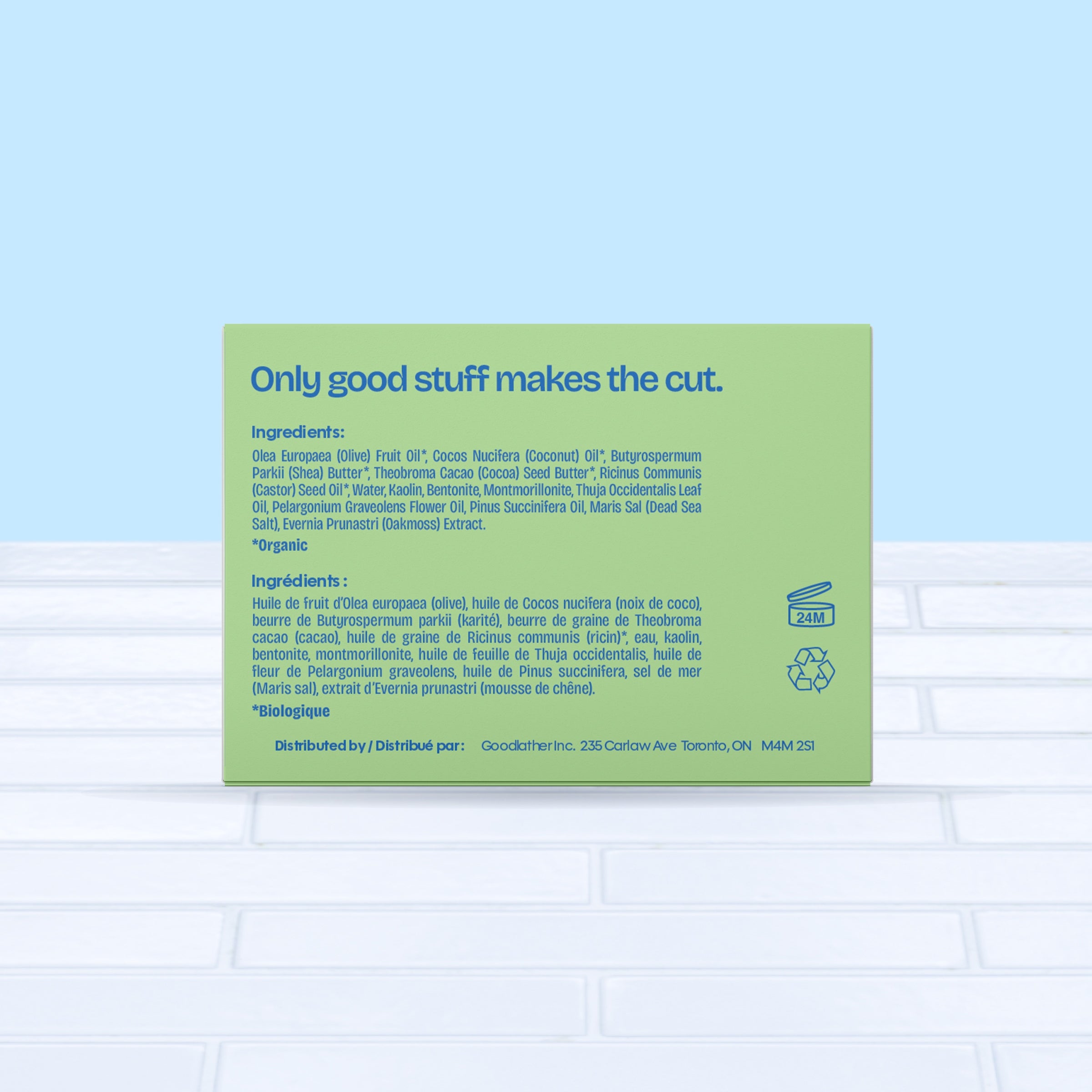 A green and bright blue Goodlather Cedar Oakmoss Bar Soap box sits on a white tiled surface, showing all natural ingredients, distribution info, and eco-friendly icons with the bilingual heading "Only good stuff makes the cut.