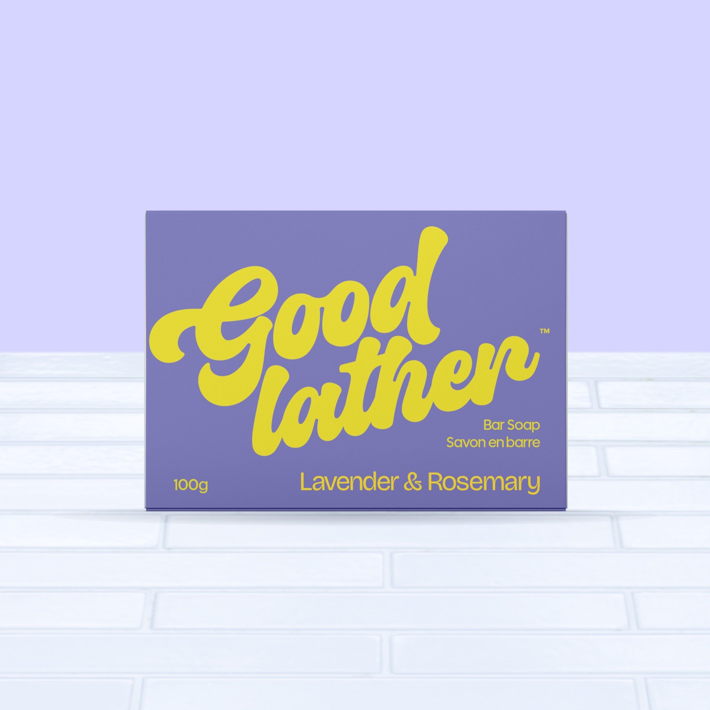 A purple and yellow box of Goodlather Lavender and Rosemary Bar Soap, made with natural ingredients, is shown on a light tiled surface against a pastel purple background.